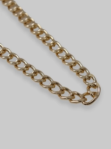 Close-up detail of golden metal Cuban chain links with premium polished finish