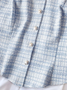 Close-up of blue tweed vest with intricate texture and decorative lion head buttons