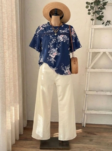 Détail d'un haut en mousseline fleurie bleu foncé avec un pantalon large blanc crème