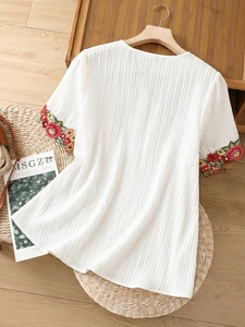 Detail of floral embroidery on sleeve with vertical pleated fabric texture of white top