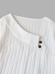 Detail of white asymmetric neckline with wooden buttons and vertical ribbed texture