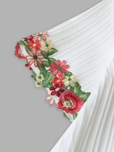 Macro shot of colorful floral embroidery and pleated fabric texture on a white summer shirt