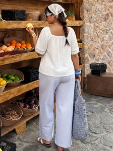Detail of white cotton eyelet lace top with intricate cutout embroidery and floral patterns
