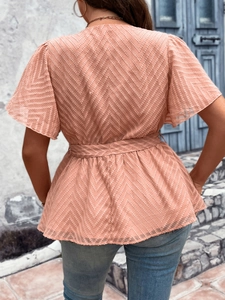 Outdoor shot of a pink chevron textured V-neck top with tie waist and ruffle sleeves