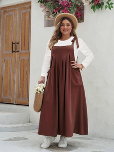 Detail of a brown sleeveless overall dress with side pockets and a white long-sleeve shirt