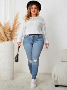 Detail view of a white long sleeve lace knit top with ruffled layers and ripped blue jeans