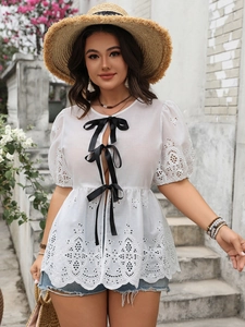 Détail du haut en dentelle blanche avec nœuds en satin noir et broderie ajourée élégante