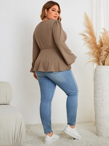 Detail view of a brown long-sleeved peplum top paired with blue jeans in a cozy setting