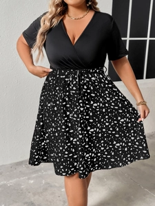 Detail of plus size V-neck dress featuring black bodice and floral print skirt with waist tie
