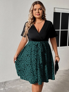 Detail of plus size V-neck dress featuring black top and green polka dot pleated skirt