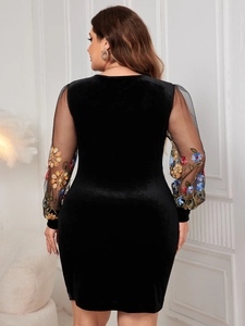 Detail view of colorful floral embroidery on black sheer mesh sleeves of a velvet dress