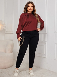 Detail of burgundy satin blouse with knotted neckline paired with black pants