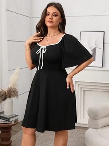 Detail of square neckline with white trim and delicate bow on black A-line dress