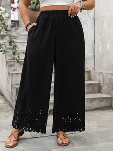 Detail of black wide-leg trousers featuring laser-cut floral patterns at the hemline