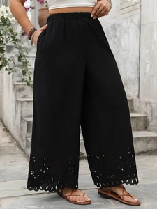 Detail of laser-cut floral patterns on black high-waisted wide-leg trousers