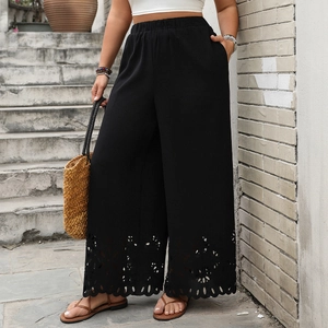 Detail of laser-cut eyelet pattern on the hem of black wide-leg trousers for women