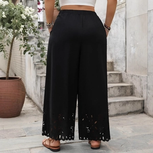 Women's black high waist wide leg pants with laser-cut floral hem detail in outdoor setting