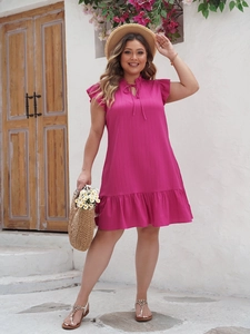 Detail of rose pink plus size dress featuring ruffle sleeves and pleated hem in sunlight