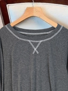 Dettaglio della maglia grigia a maniche lunghe con cucitura decorativa a X sul collo