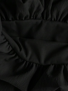 Nahaufnahme von schwarzem Rippstoff mit gerafften Rüschendetails an einem A-Linien-Kleid