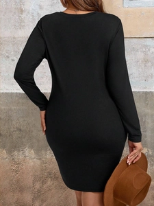 Elegant plus-size black long-sleeve dress shown from the back against a vintage wall