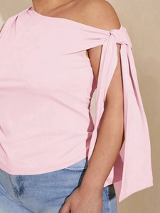 Pink one-shoulder top with knot detail and long ribbons paired with denim jeans