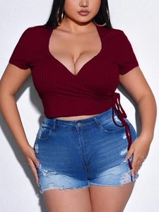Plus size deep V-neck wrap top in burgundy ribbed knit paired with ripped denim shorts