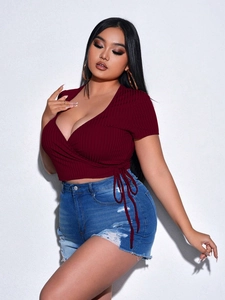 Detail of burgundy V-neck ribbed knit top with side bow tie and distressed denim shorts