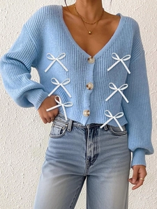 Détail du cardigan bleu clair avec nœuds en ruban blanc et boutons marbrés marrons