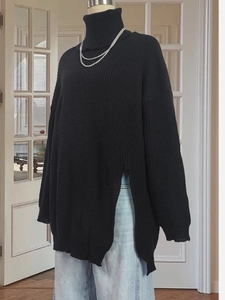 Detailed close-up of chunky black knit sweater with side slits and oversized turtleneck