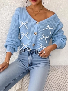 Gilet en maille bleu à col en V avec nœuds blancs et boutons en bois sur jean