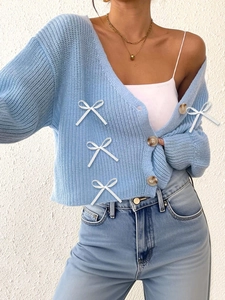 Vue détaillée du cardigan en maille bleu avec des nœuds blancs et des boutons marron texturés