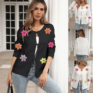 Detail of a tie-front knit cardigan featuring colorful 3D crochet floral appliques and bows