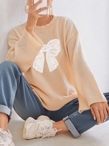 Close-up of apricot long sleeve sweater featuring a large white lace bow and ribbed cuffs