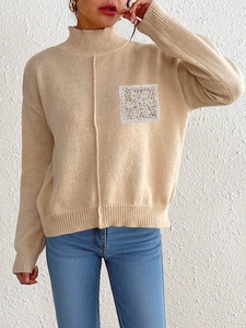 Detail of beige knit sweater featuring a white lace crochet pocket patch and mock neck