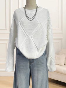 Close-up of white oversized cable knit sweater with geometric diamond texture and ribbed cuffs