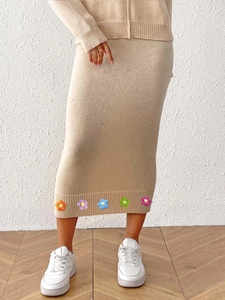Detail of colorful 3D crochet flower patches on the hem of a beige knit pencil skirt
