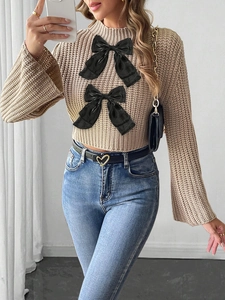 Detail of beige knit sweater with black satin bows and bell sleeves paired with denim