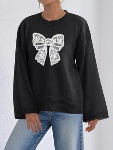 Detail of black knit sweater featuring a large white lace bow and elegant flared sleeves