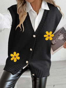 Détail du gilet en maille noire avec boutons perlés et appliques de fleurs jaunes
