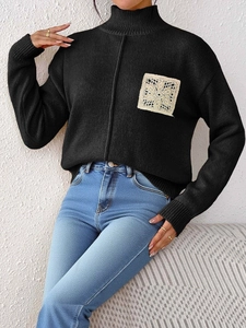 Detail of black knit sweater featuring white floral crochet lace patch on the chest