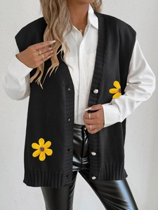 Détail de gilet noir en maille avec fleurs jaunes au crochet et boutons perlés