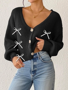 Détail du cardigan en grosse maille avec col en V profond et nœuds blancs décoratifs