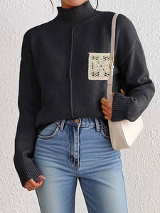 Close-up of black high-neck sweater with white floral lace patch on the chest detail