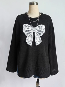 Detail of black knit sweater featuring a large white lace bow and round neckline