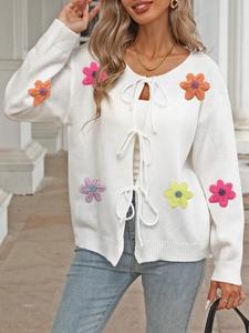 Close-up of white knitted cardigan featuring colorful crochet flowers and ribbon tie closure