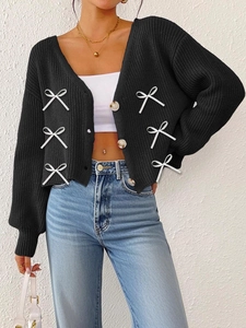 Détail du cardigan noir tricoté avec des nœuds blancs et des boutons ambrés