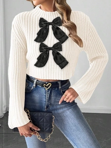 Close-up of white cable knit crop sweater featuring two large black decorative bows