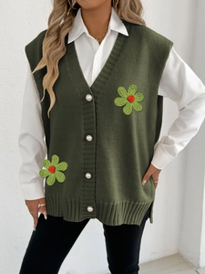 Détail de boutons perle et de fleurs tissées sur un gilet en tricot vert foncé