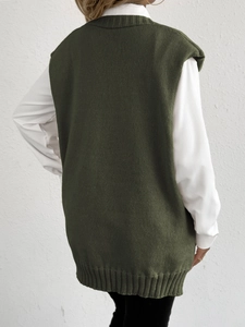 Women's dark green oversized knit vest sweater with ribbed hem layered over a white shirt
